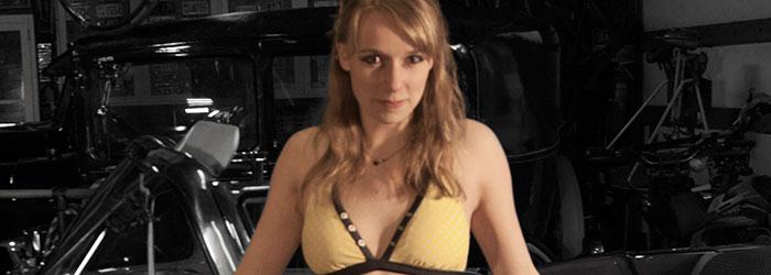 View from the waist up of a young lady wearing a bikini top, leaning on a car